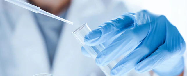 Pracownik laboratorium w rękawiczkach ochronnych przelewa badaną substancję do szklanej fiolki.